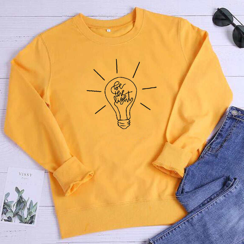 Yellow sweatshirt with a light bulb design on a white surface with jeans and sunglasses.